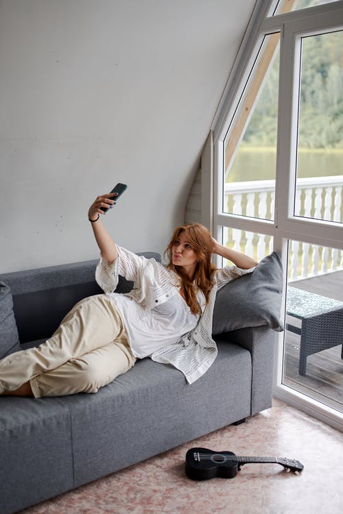 Frau macht Selfie auf grauem Sofa